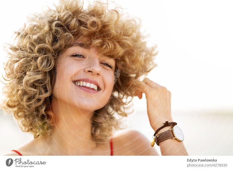 Portrait of young woman with curly hair smiling millennials urban street city stylish people young adult casual attractive female happy Caucasian toothy
