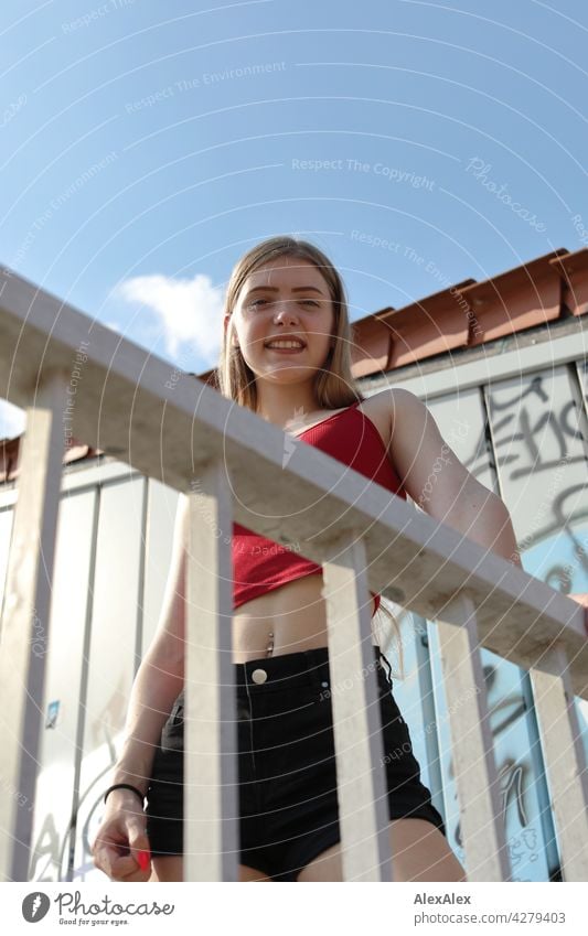 Young woman in hot pants and red top holds on to a railing and looks down Woman Blonde Black Pink Long-haired portrait Wall (building) 18 - 30 years 18-25 years