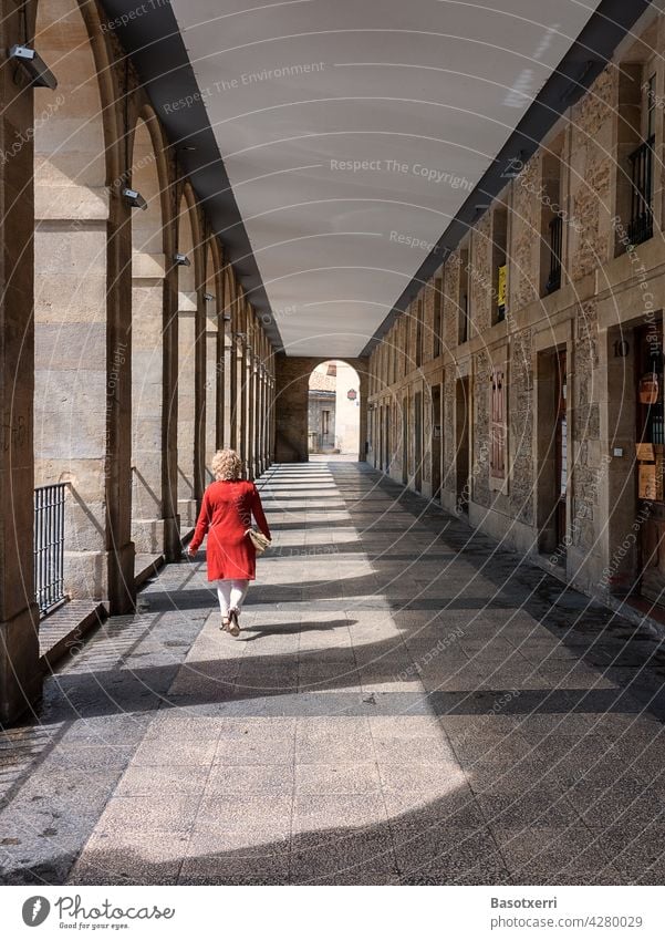 Woman in red coat crosses arcade in old town. Los Arquillos, Vitoria-Gasteiz, Basque Country, Spain Vitoria Gasteiz Arcade passage Red Arch Corridor archway
