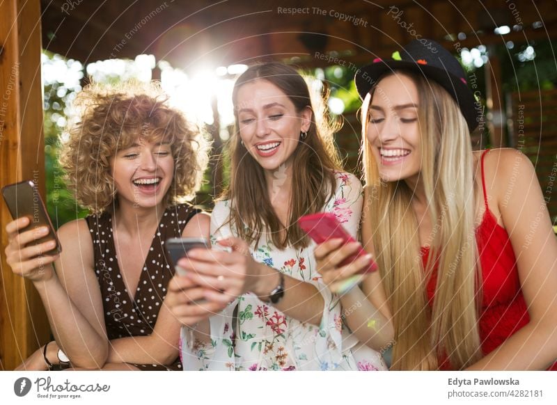 Happy young women having fun with smartphones sunset summer group together people woman casual beautiful attractive girl girls female three people friends