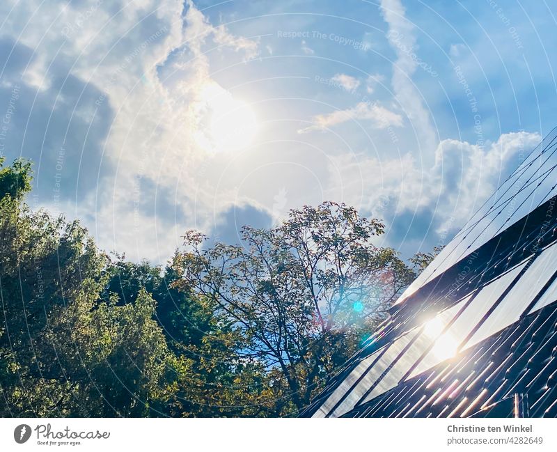 The sun shines brightly from the slightly cloudy sky and is reflected in the collectors of the solar system and the photovoltaic system of a residential house.