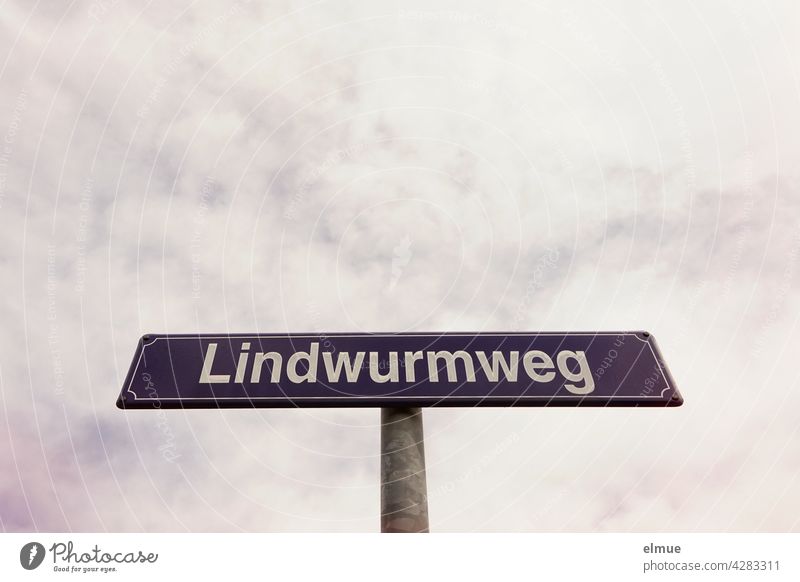 purple street name sign with white writing " Lindwurmweg " in front of cloudy sky / orientation street sign Street sign lindworm unusual street names dragon