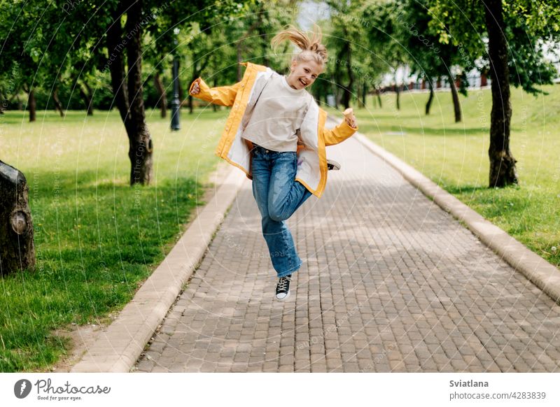 A teenage girl walking in the park jumping with ice cream in her hands. Child outdoors summer teenager back view funny trend blonde happy cute child kid little