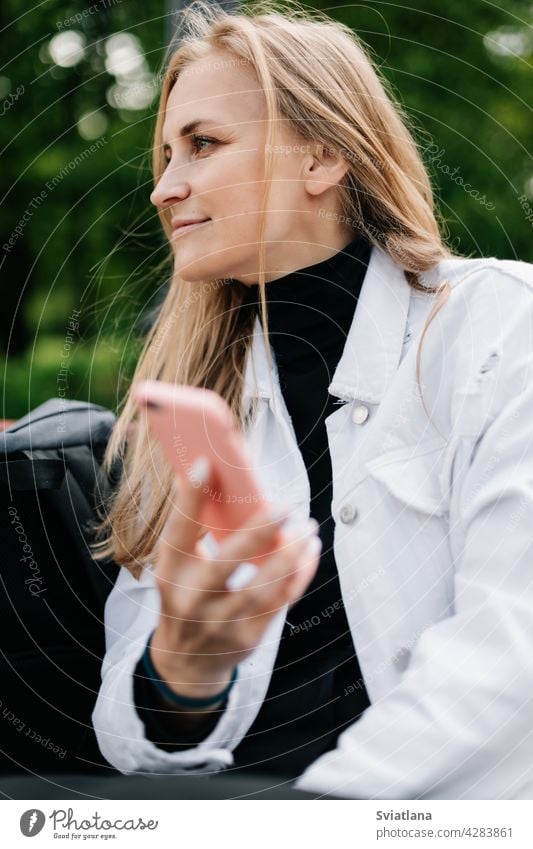 Happy blonde sitting on a bench in a city park, talking on the phone and texting with friends woman lifestyle young people mobile communication smartphone