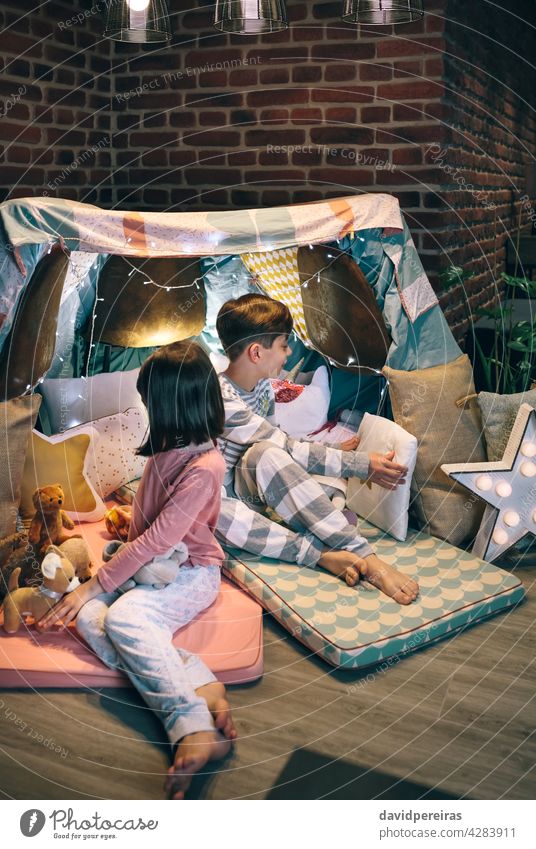 Children preparing tent with chairs and bed sheets children teepee pajama party decoration placing cushions stuffed dolls home collaborate cozy house brother