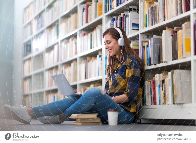 Female college student sitting in a library using a laptop enjoying lifestyle young adult people one person casual caucasian positive happy smiling woman female