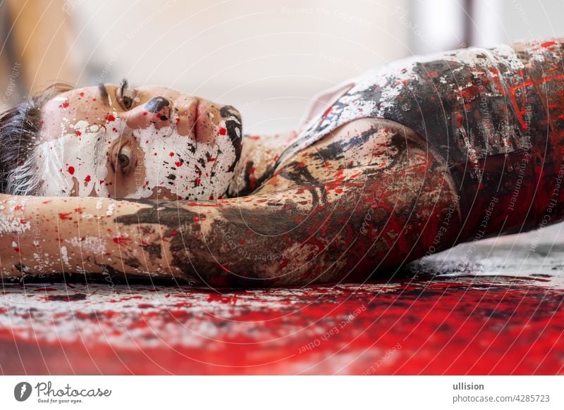 young and sexy Woman in underwear, sportswear, artistically abstract painted with white, red and black paint, lying on the colorful painted floor in the studio, copy space.