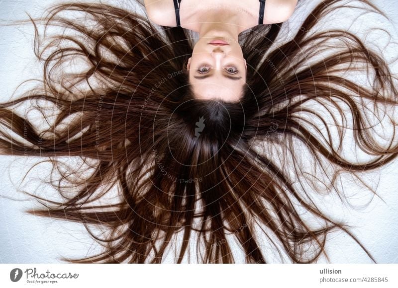 Beautiful young woman lying on the white background with long widespread sprawled hair brown fashion haircare vogue brunette wave silky styling sexy cute beauty