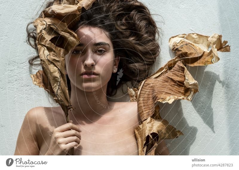 Portrait of a young sexy woman with brown hair artfully decorated between leaves of dry, withered banana tree looking like an art nouveau girl, copy space.
