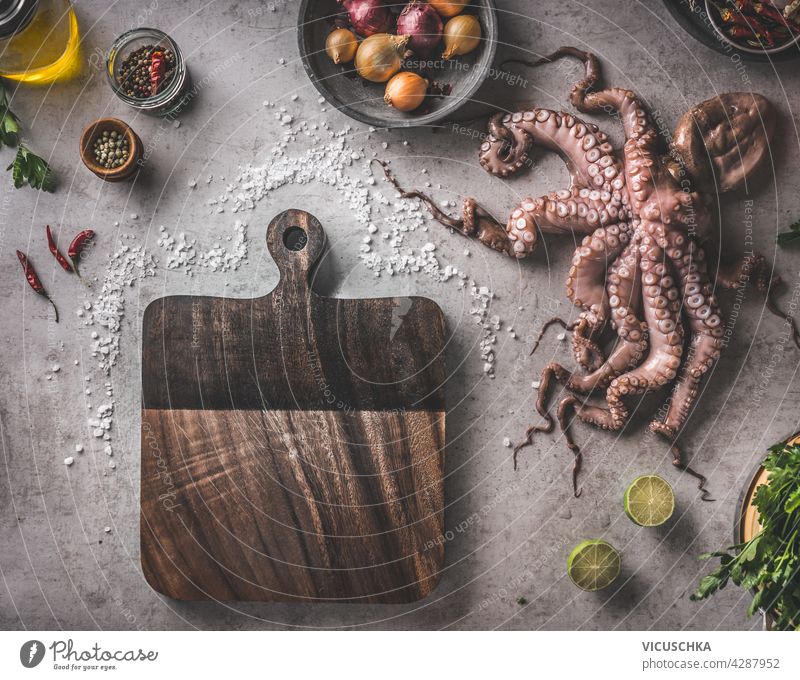 Mediterranean food concept with uncooked octopus, spices, vegetables and herbs. Cooking preparation with fresh ingredients and equipment. Rustic cutting board on grey concrete background. Top view