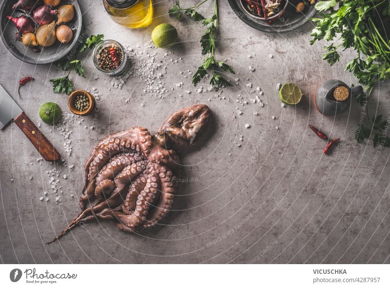 Cooking preparation of Octopus with fresh ingredients and kitchen equipment , herbs, lime, onion, salt, spices. Fresh food concept on dark concrete background. Top view