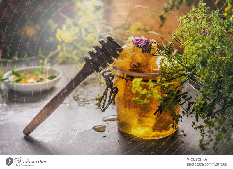 Closeup of jar with honey and honey spoon and wild flowers. Bowl with honey in background. Natural food concept. Dark concrete background. Front view. closeup