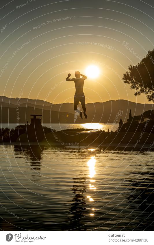 Teen jumps from diving board into the water in the evening Evening Sunset pool Boy (child) teenager Springboard Back-light Backlight shot Water Swimming pool
