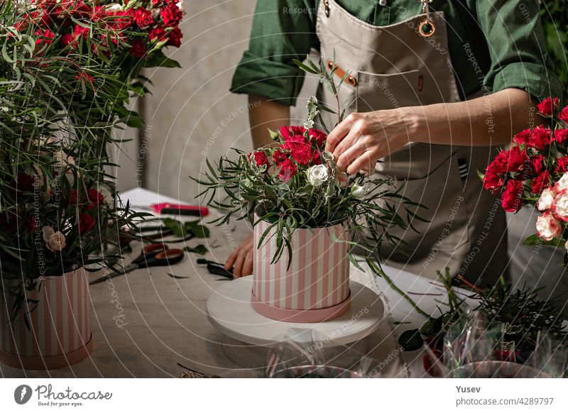 Florist make gift bouquets in hat boxes. Graceful female hands make a beautiful bouquet. Florist workplace. Small business concept. Front view. Flowers and accessories