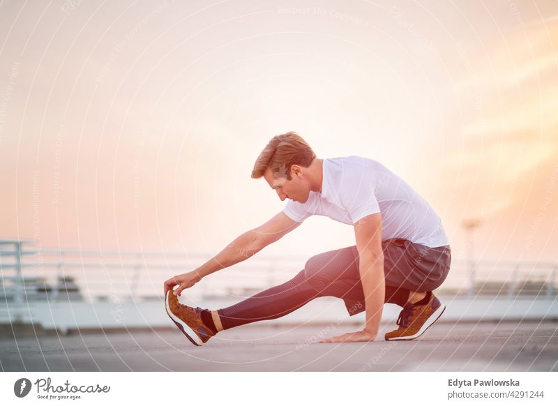 Young man doing stretching exercise in urban area Jogger runner jogging running people young male energy clothing exercising fitness recreation sport