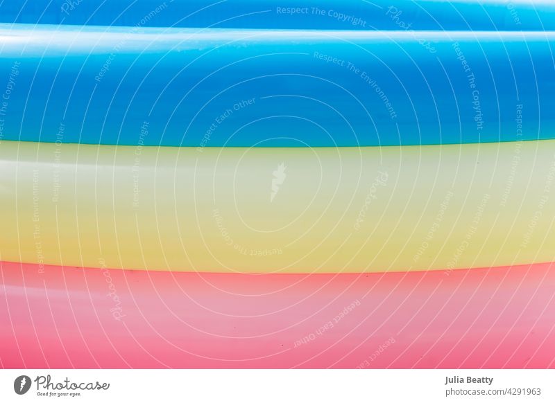 Summer: closeup of the side of blow up pool with blue, yellow, and pink rings summer inflated round puffy traditional candy bright faded abstract pride lgbtq