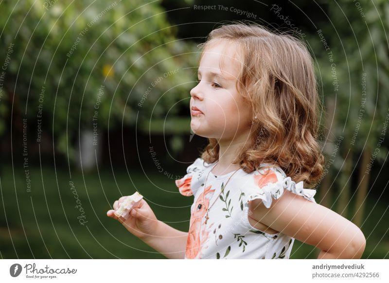 Funny kid girl eating sandwich outdoors. Having fun. Looking at camera. Posing over nature background. Healthy food. Childhood. happy little lifestyle childhood