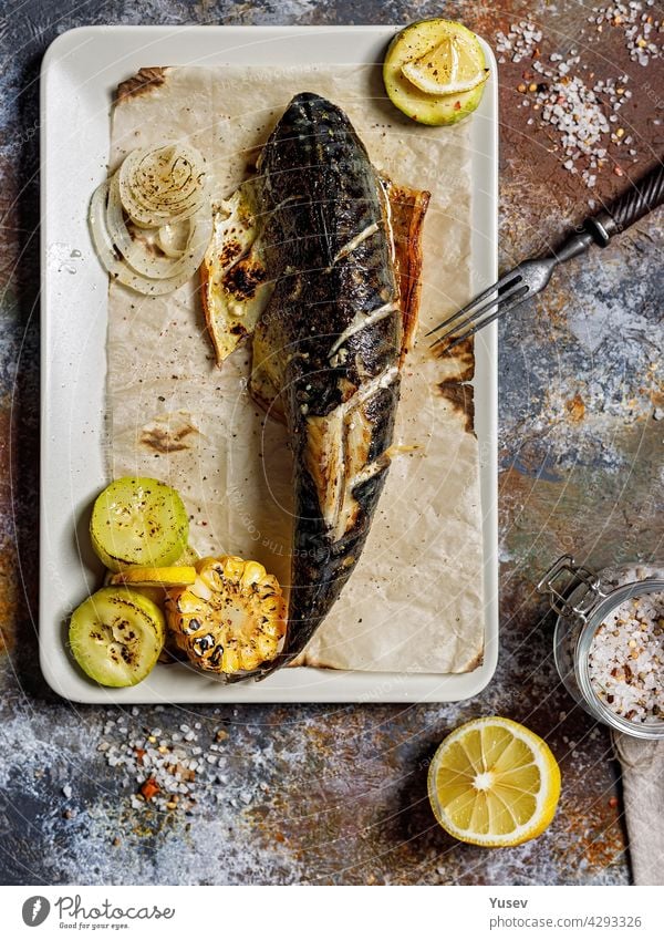 Top view delicious grilled mackerel with vegetables on a rectangular plate. Appetizing roasted sea fish with corn, zucchini and spiced lemon. Mediterranean Kitchen. Healthy seafood. Vertical shot
