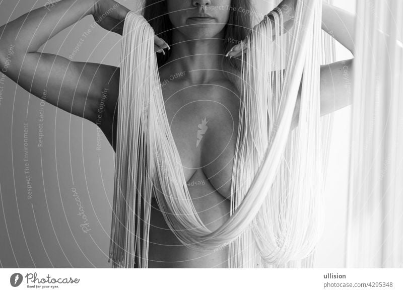 Attractive sexy nude body, chin and mouth of a young woman, partially obscured by the white threads of a falling string curtain decorative in elegant shapes.