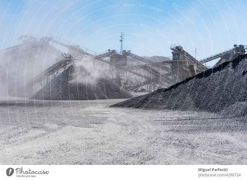 Arid quarry with moving mechanical belt line to separate gravel by size, all wrapped in a cloud of dust. conveyor sand and gravel gravel pit arid construction