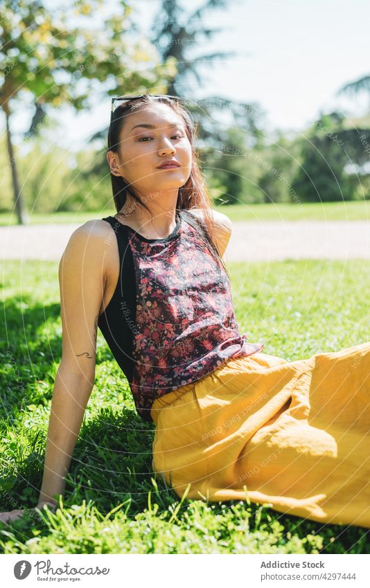 Gentle Asian woman resting on lawn in park dreamy gentle feminine charming pleasant summertime meadow portrait contemplate ornament tattoo romantic harmony