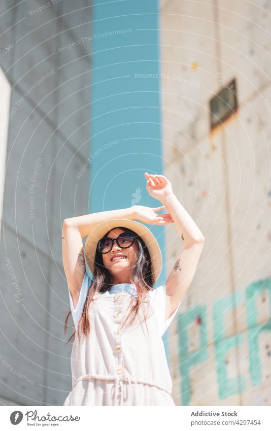 Stylish Asian woman in sunglasses in town content tattoo style romantic individuality lifestyle arm raised cheerful hat smile enjoy summer asian ethnic white