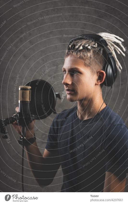 Vertical shot stilysh guy with dreadlocks is recording a song in the studio. A young attractive singer in black studio headphones stands in front of a microphone and sings. Generation Z young talent