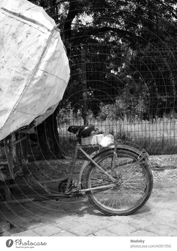 Old cargo bike with huge garbage bag in summer sunshine on the roadside in Adapazari in Sakarya province, Turkey, photographed in neo-realistic black and white