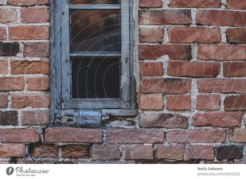 One glass window on old red brick wall. Vintage window in white wooden frame on red brick wall of industrial building. Jar of glass lying on windowsill. jar