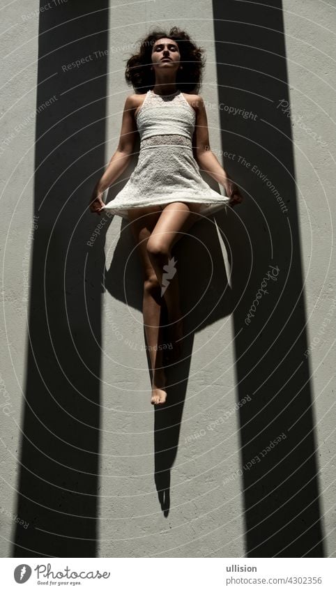 young sexy woman lies between two black shadow stripes on the floor in the sun and casts a strong shadow Woman dress dark white mysterious mystery light glamour
