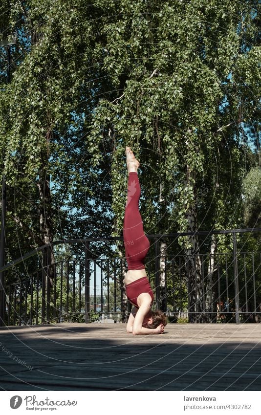 Young brunette woman practicing Salamba Sirsasana Headstand pose in the park on wooden platform Headstand. yoga balance outdoors yogini sport athletic female