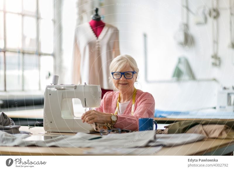 Senior fashion designer using a sewing machine in her workshop Sewing Machine Cloth Fabric Material dressmaker seamstress tailor clothing indoors woman female