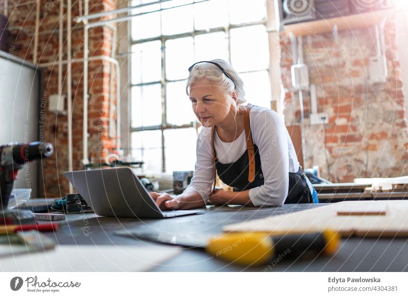 Senior woman using laptop in her workshop indoors female mechanic owner profession service small business employee working technician workplace manual worker