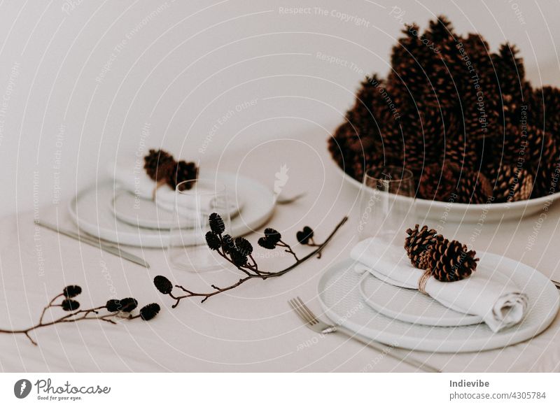 A big bowl of pine cones on a Christmas dinner table with plates and glasses for stylish holiday decoration christmas meal cutlery family supper food festive