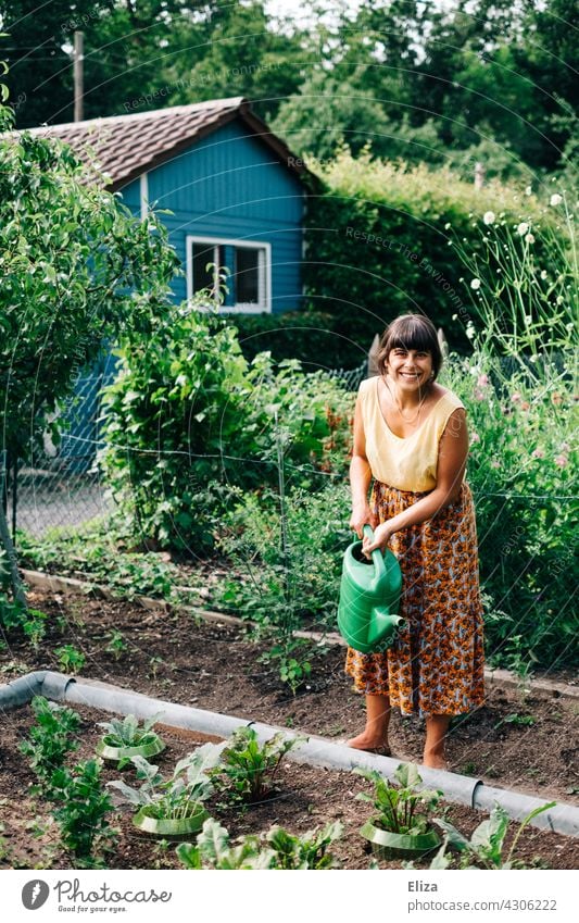 Woman watering the vegetable beds in the allotment garden with a watering can Garden Cast Gardening Watering can Nature Summer gardener variegated cheerful
