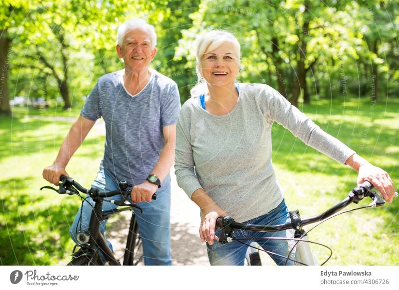 Senior Couple Riding Bikes In Park bicycle bike senior seniors pensioner pensioners casual outdoors day Caucasian happiness toothy smiling enjoying summer