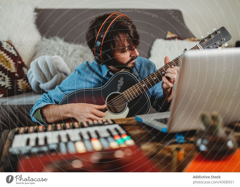 Musician playing on guitar near laptop at home a Royalty Free