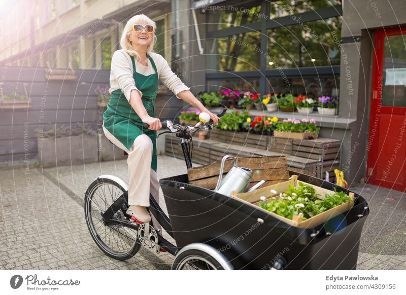 Happy owner of a flower shop using cargo bike bicycle cycling transport commuting delivery Florist people adult senior mature woman female smiling happy apron