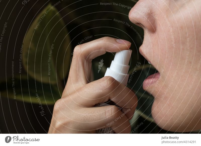 Woman taking homeopathic oral spray; background has ficus house plants natural homeopathy health fast absorption mouth remedy therapeutic immune system