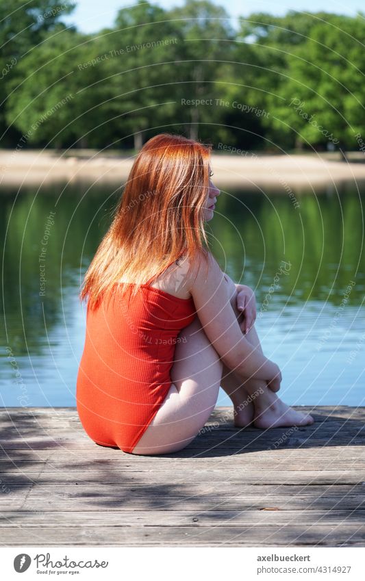 young woman in red bathing suit sits on wooden pier at bathing pond Young woman Swimsuit Swimming lake Summer Swimming & Bathing Water Lake Vacation & Travel