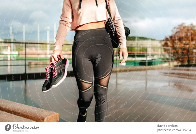 Unrecognizable sportswoman with gym bag and sports shoes walking to go to training unrecognizable athlete midsection crop top holding sneakers wet floor rainy