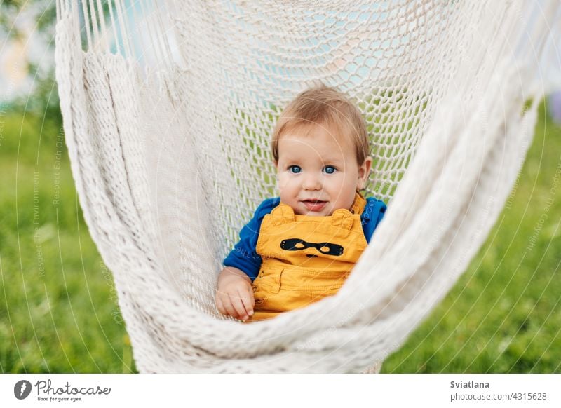 A little boy sits in a hammock and looks at the camera on a summer day in the garden baby toddler child sun green nature summertime sunbathing relax outside
