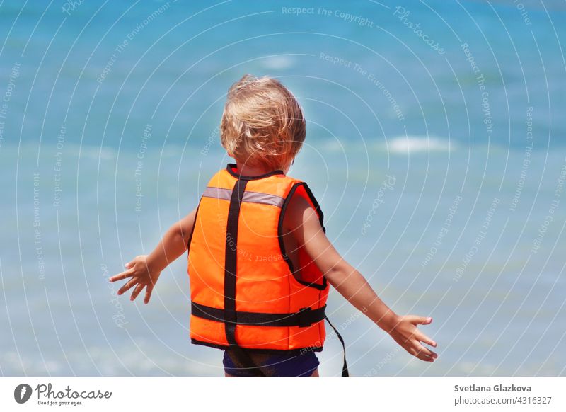 Safety of life concept. Little caucasian boy uses a life jacket on a summer beach against the backdrop of the sea waves. caucasian boy beach safety of life