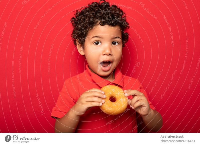 Cute boy eating donut in studio child doughnut kid sweet tasty dessert treat delicious food hungry childhood yummy cute pastry enjoy confectionery curly hair
