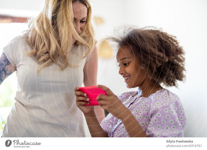 Young girl showing her mother something on a smartphone child family daughter multi-ethnic mixed race family diverse family diversity afro home real people