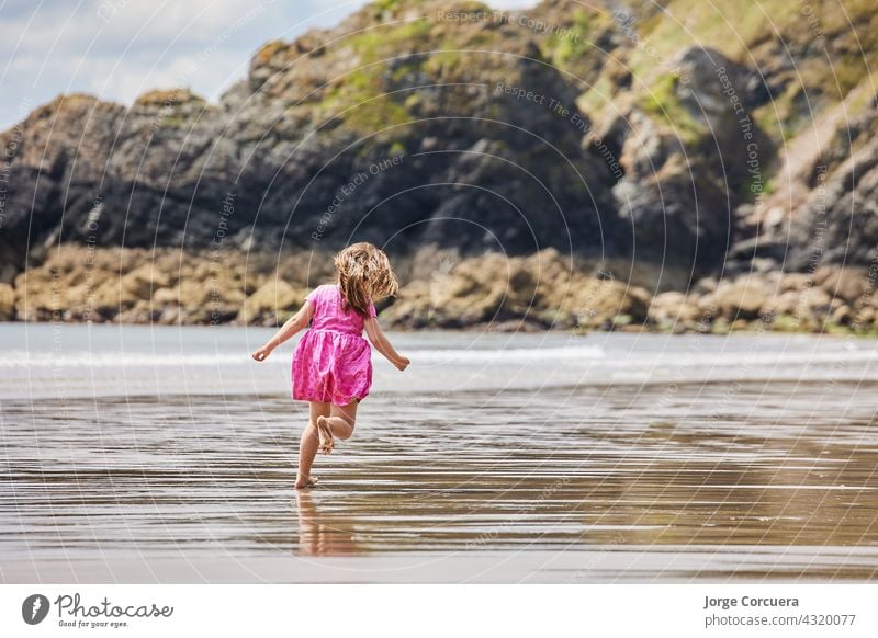 Hispanic girl running along the beach with big rocks in the background sand playing adorable toddler kid summer young child childhood sea person cute caucasian