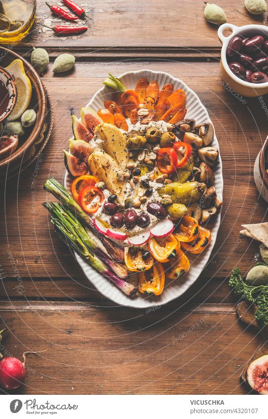 Plate with freshly homemade hummus, grilled vegetables and a variety of nuts and seeds toppings. Healthy vegan food. Lunch or snack on rustic wooden background. Top view