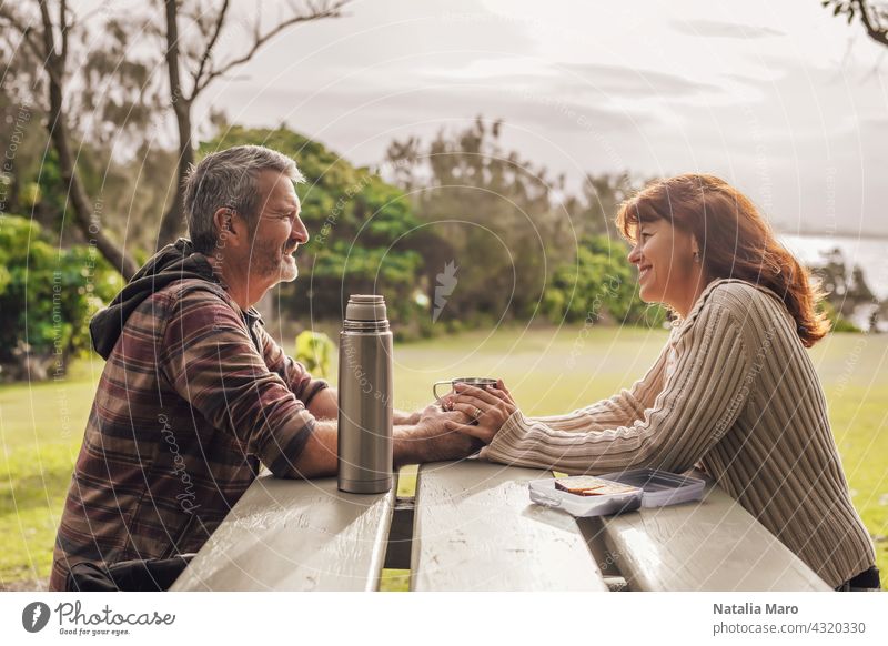 Middle-aged couple sitting on the benches with table in park and drinking tea. middle-aged woman happy ocean together leisure love adult pretty relationship