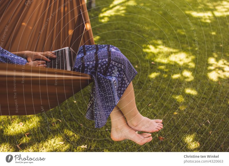 A young woman in a blue summer dress sits comfortably in a hammock in the garden, works on the notebook and lets her feet dangle Woman Young woman Hammock Cozy