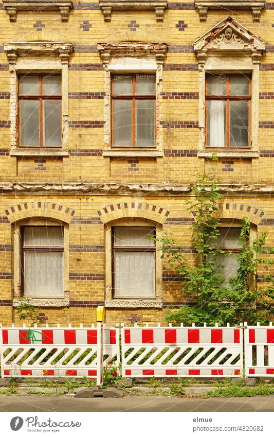 red-white barrier beacons in front of a richly decorated but slowly decaying residential house with yellow-brown clinker facade from the Gründerzeit / dilapidated / lost place